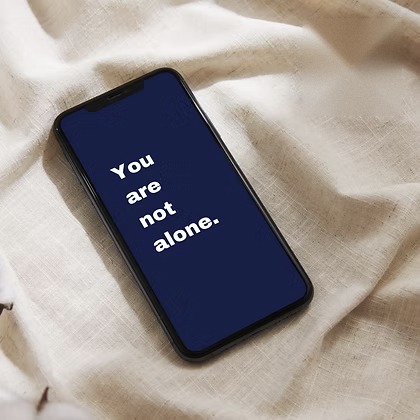 Phone on linen with a navy screen reading &ldquo;You are not alone.&rdquo;