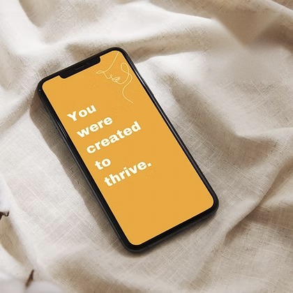 Phone on linen with a gold screen reading &ldquo;You were created to thrive.&rdquo;