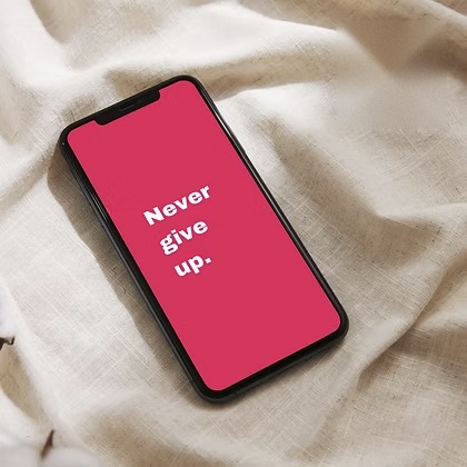 Phone on linen with a pink screen reading &ldquo;Never give up.&rdquo;