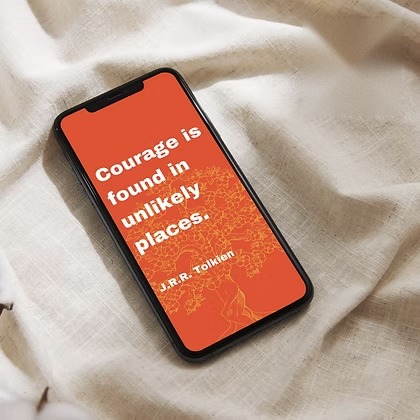 Phone on linen with an orange screen quoting J.R.R. Tolkien: &ldquo;Courage is found in unlikely places.&rdquo;